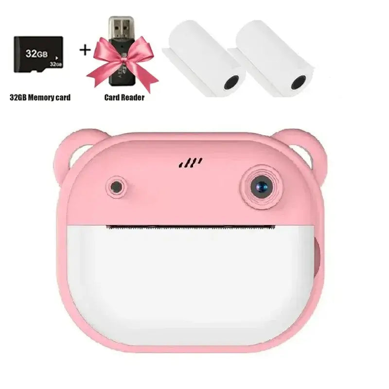Children's digital instant print camera in pink with 32GB memory card, card reader, and thermal paper rolls.